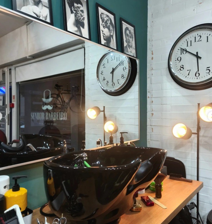 Interior da barbearia Senhor Barbeiro com lavatórios, espelhos e relógios